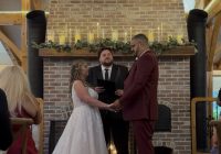 "Fireside fall vineyard wedding ceremony at Zorvino Vineyards: Emily Arsenault and Adrian Gonzalez hold hands before a candlelit brick fireplace beneath a Mr. and Mrs. Gonzalez monogram"