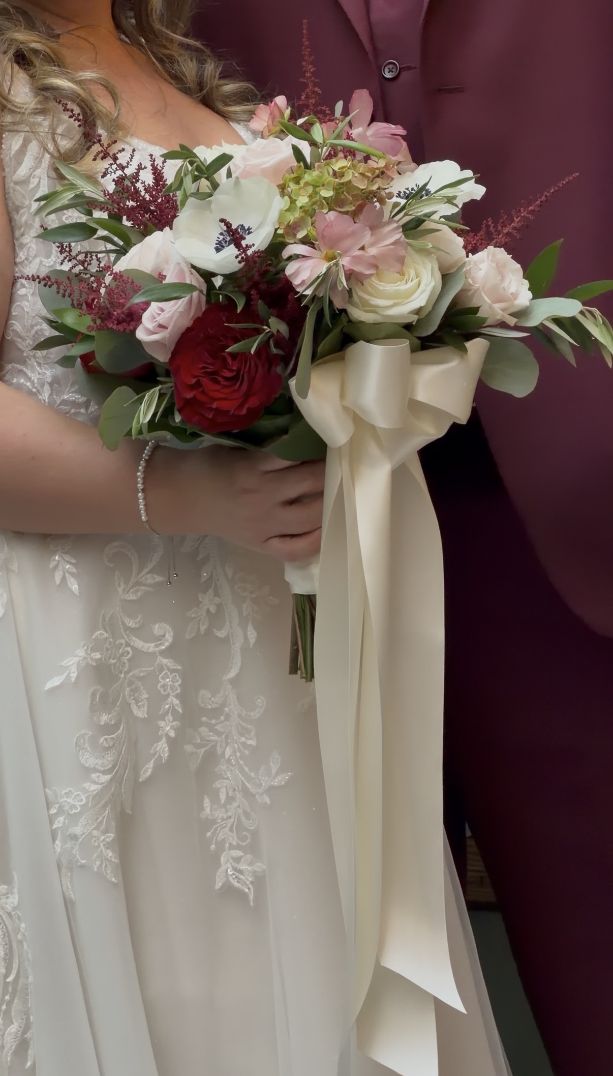 "Bridal bouquet of a red garden rose, burgundy astilbe, white anemones, blush and ivory roses, and green hydrangea tied with ivory satin ribbon"

