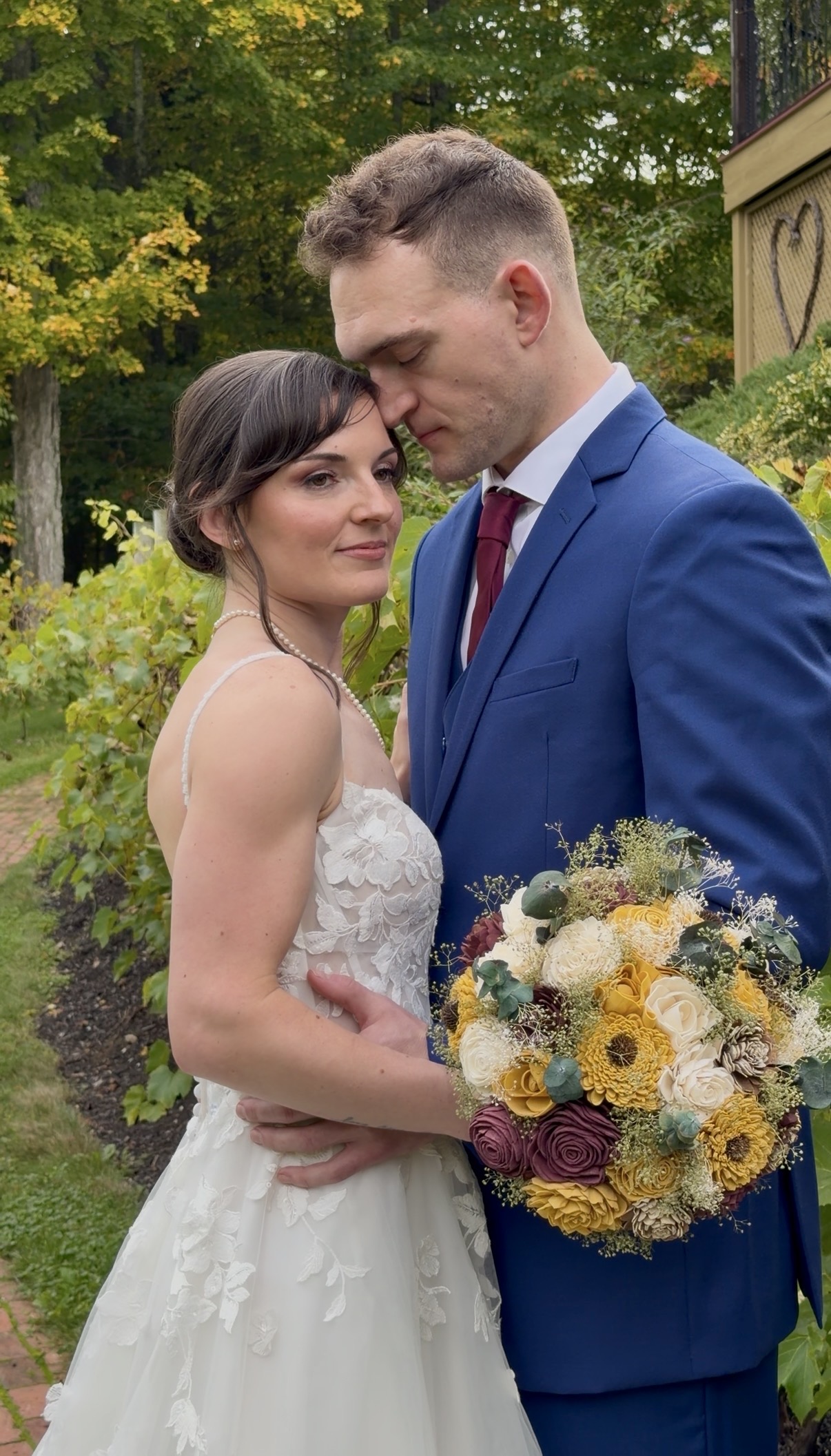 "Courtney holds a bouquet of mustard sunflowers, burgundy roses, and ivory roses as Andrew rests his head against hers beside the Zorvino vineyard rows"