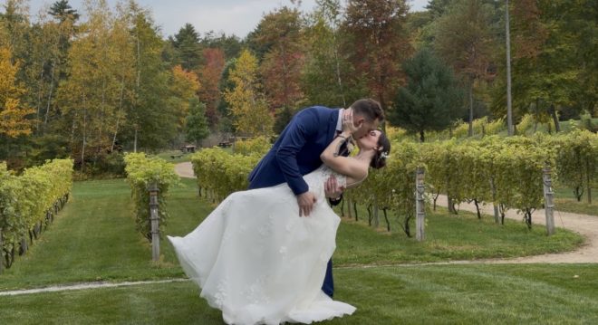 "Weekday vineyard wedding at Zorvino Vineyards: Andrew dips Courtney for a kiss between the vineyard rows as October foliage turns gold and red behind them"