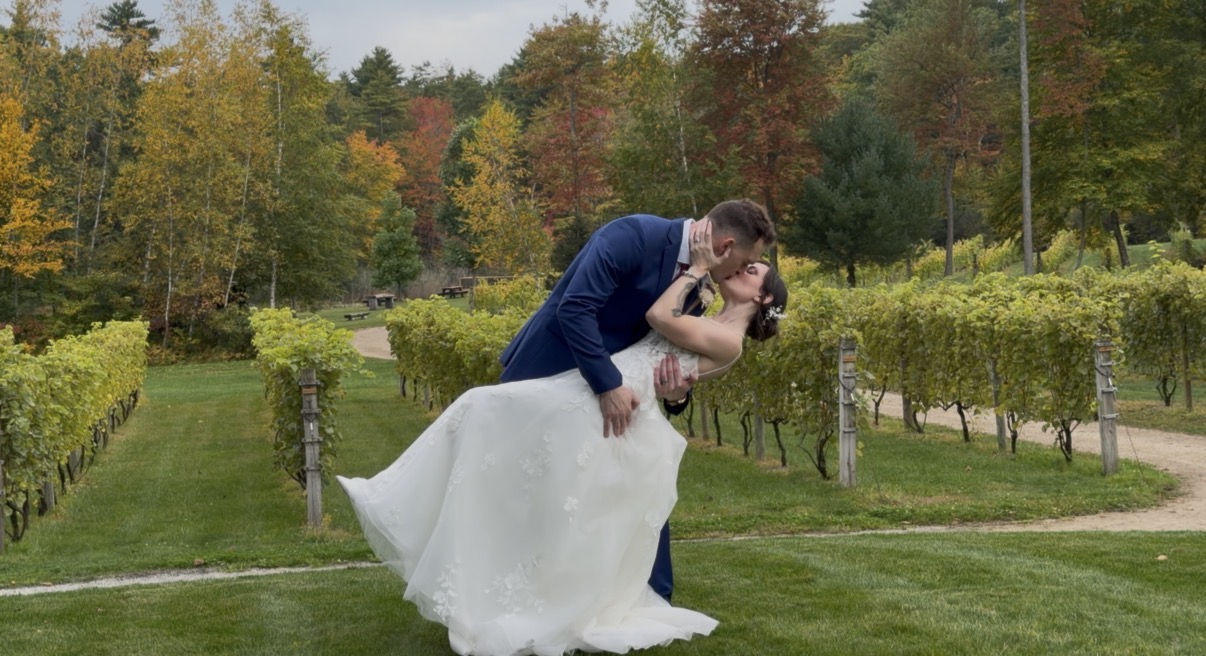 "Weekday vineyard wedding at Zorvino Vineyards: Andrew dips Courtney for a kiss between the vineyard rows as October foliage turns gold and red behind them"