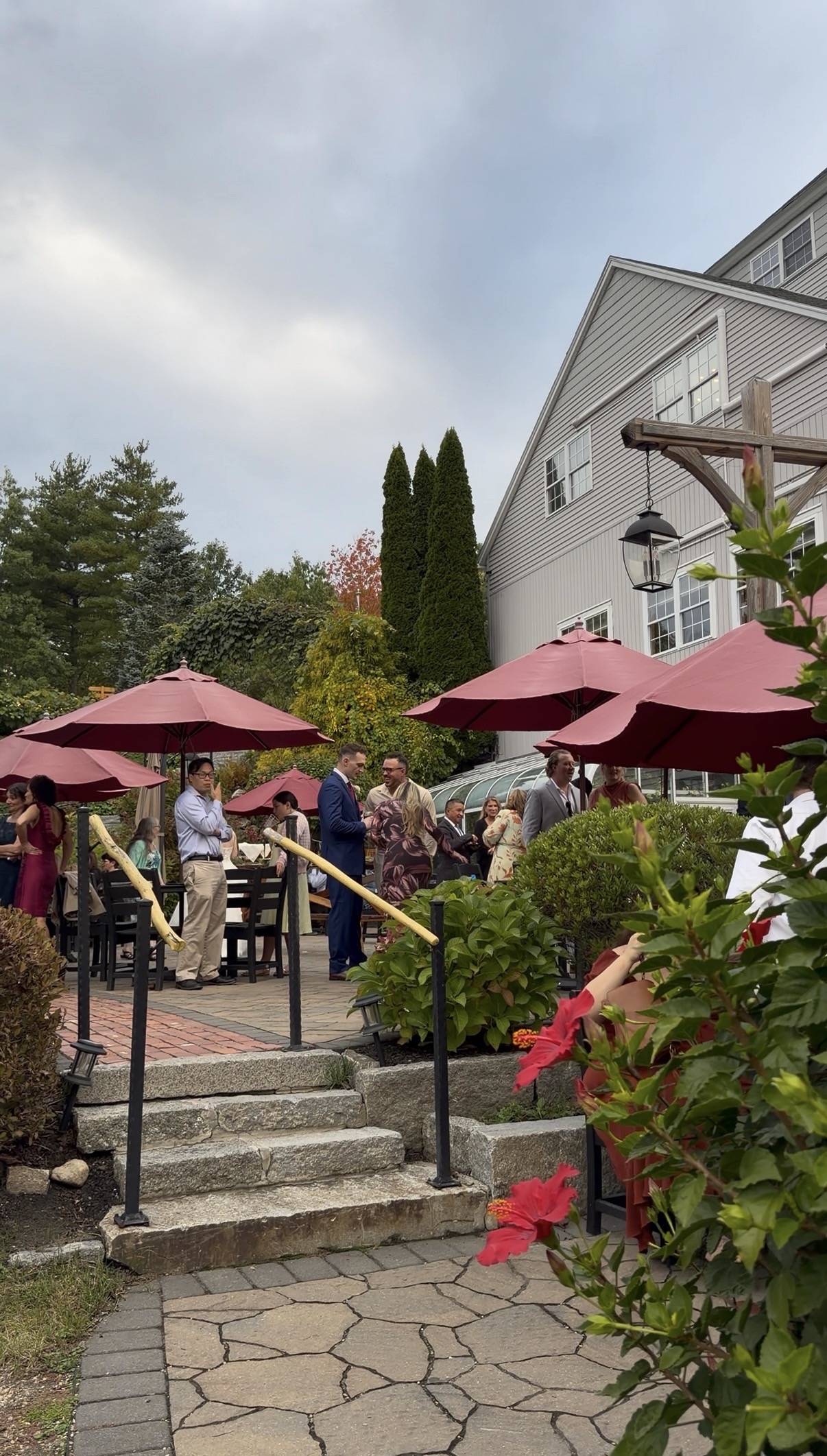"Wedding guests mingle under burgundy umbrellas on the stone patio at Zorvino Vineyards during an October cocktail hour"