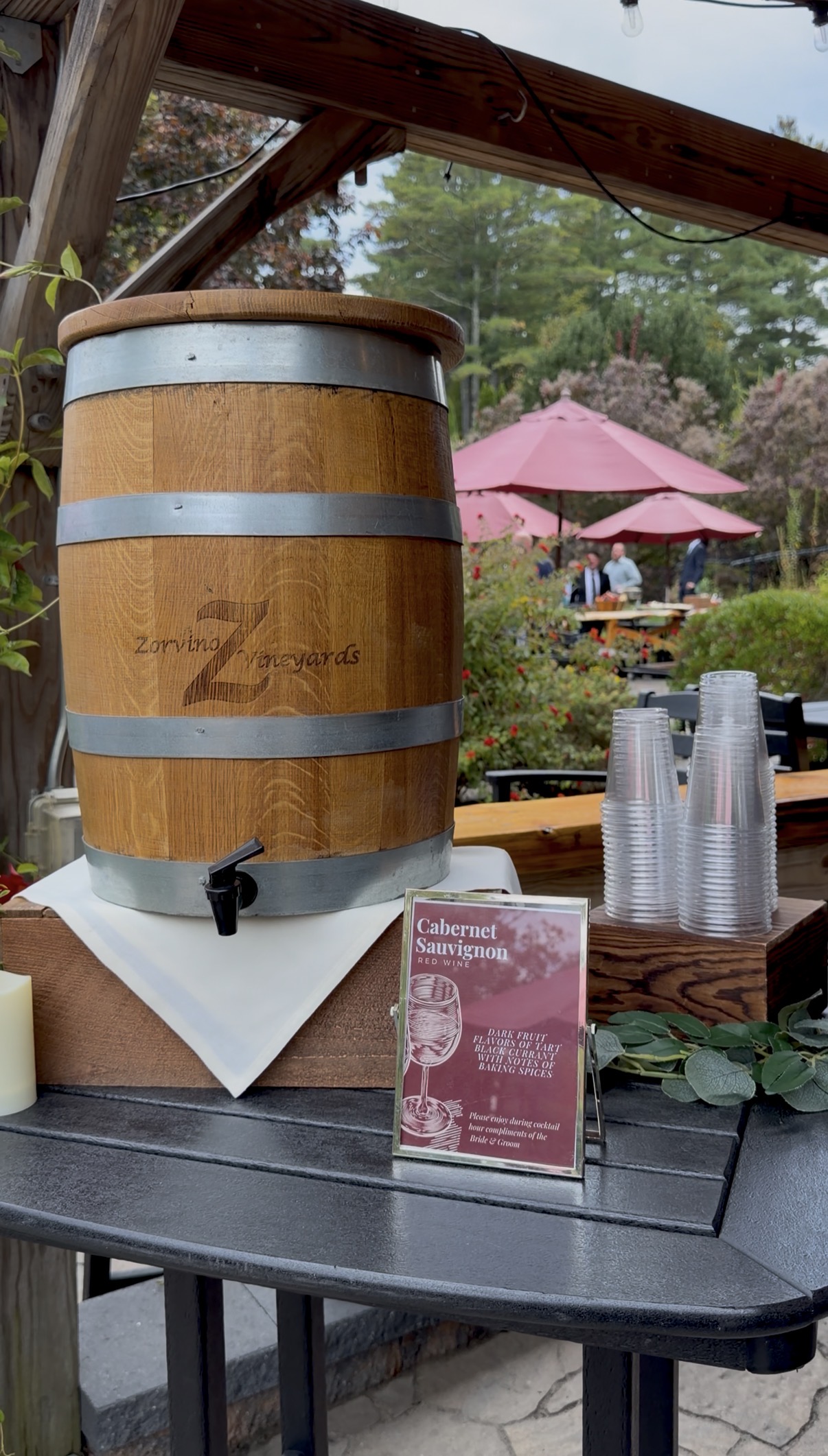 "Zorvino Vineyards oak wine barrel with a spigot beside a Cabernet Sauvignon tasting note sign and stacked cups at an outdoor wedding cocktail hour"