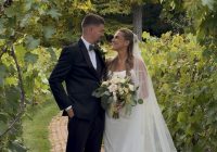 "Fall wedding at Zorvino Vineyards: Sophia Holman and Scott Donahue smile at each other on a brick path beneath a grapevine arbor in October"