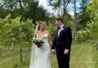 A bride and groom smile and look at each other in a beautiful green vineyard.