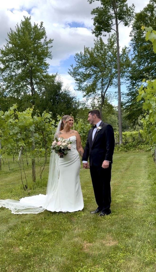 A bride and groom smile and look at each other in a beautiful green vineyard.