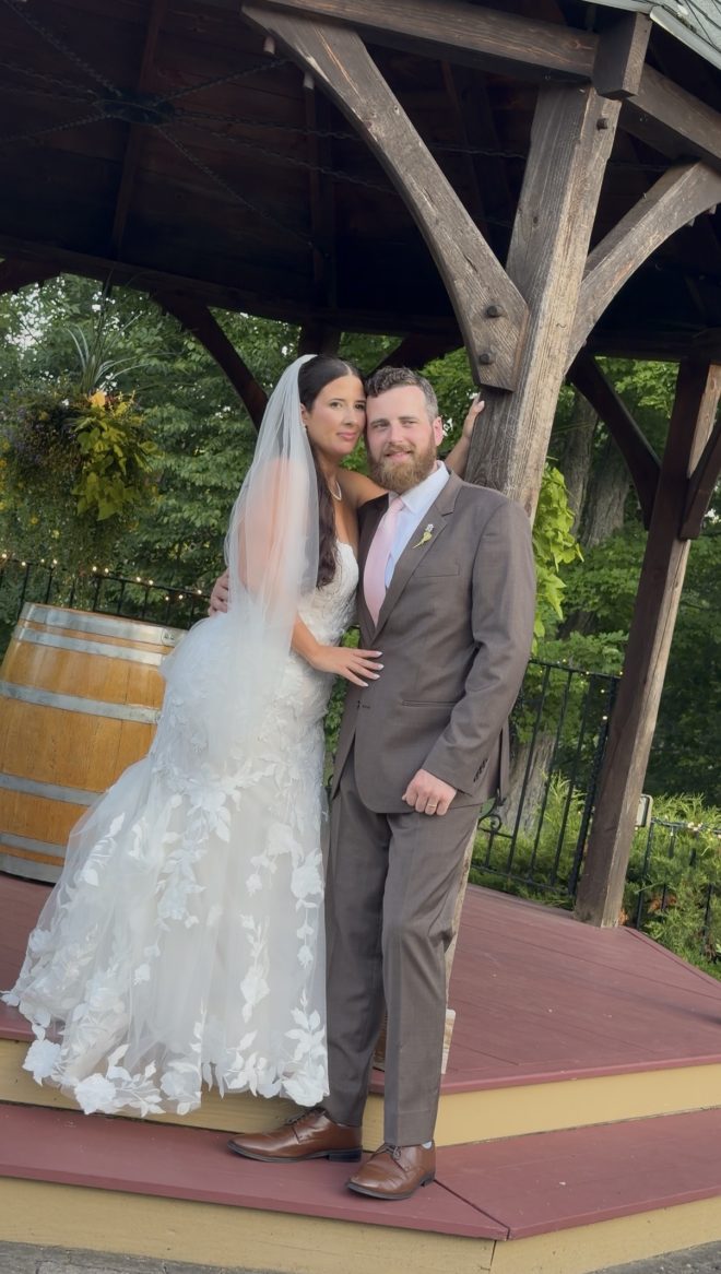 A bride and groom pose for the camera at the gazebo.