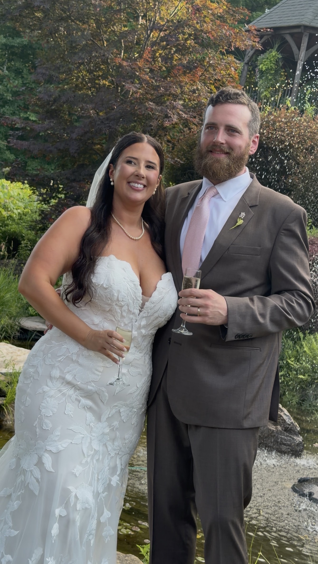 A bride and groom hold champagne glasses and smile.