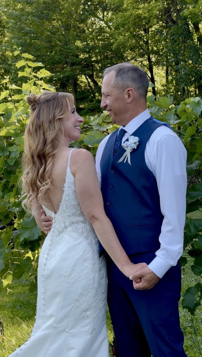 A bride and groom hold hands as they face each other, smiling.