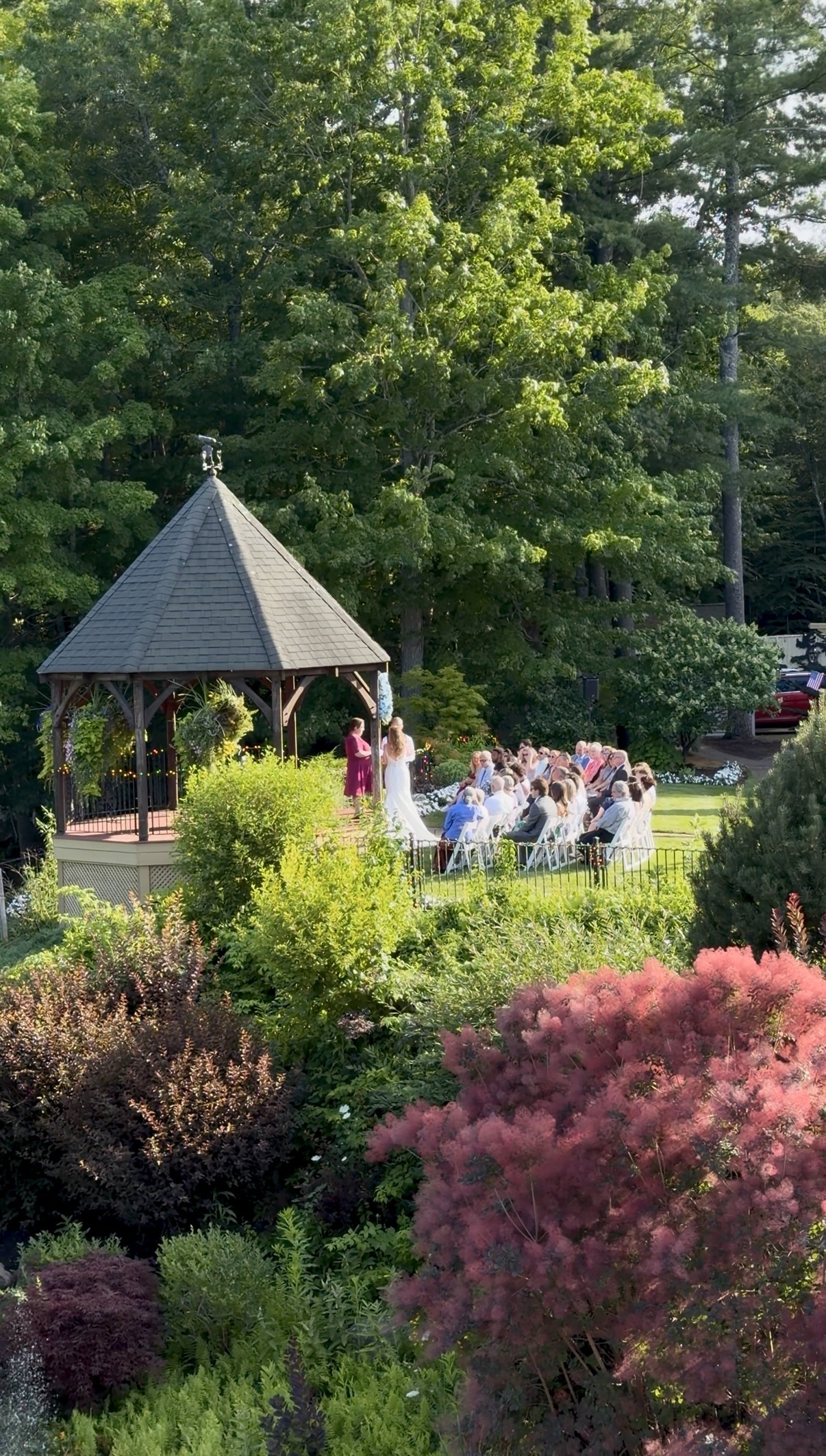 A bride and groom at the altar in front of the gazebo with guests watching the ceremony.