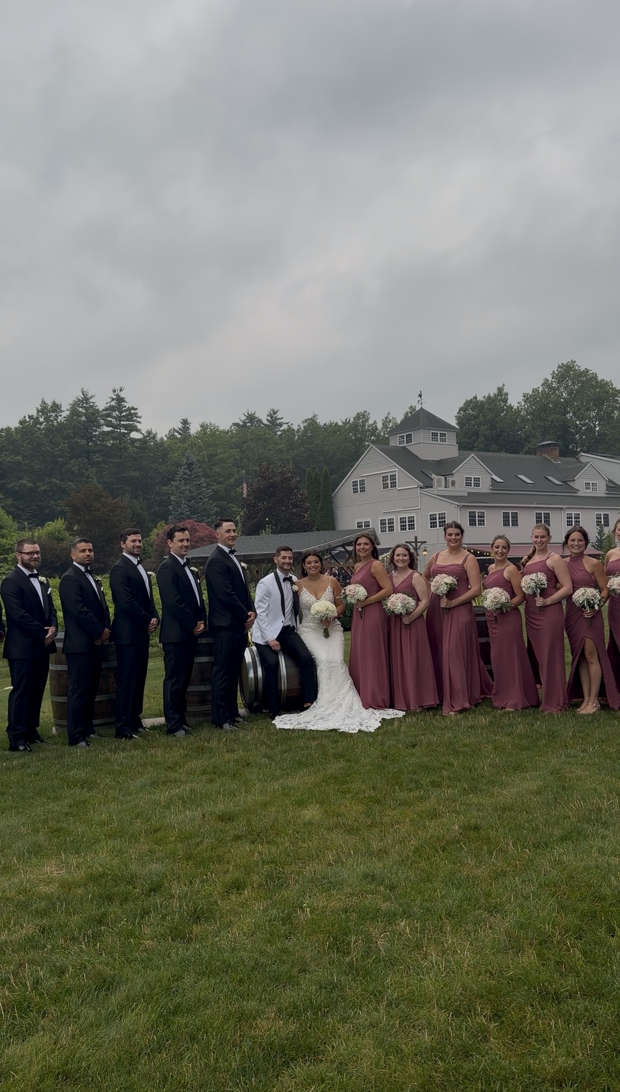 Bride and groom sit on a barrel surrounded by their bridesmaids and groomsmen.