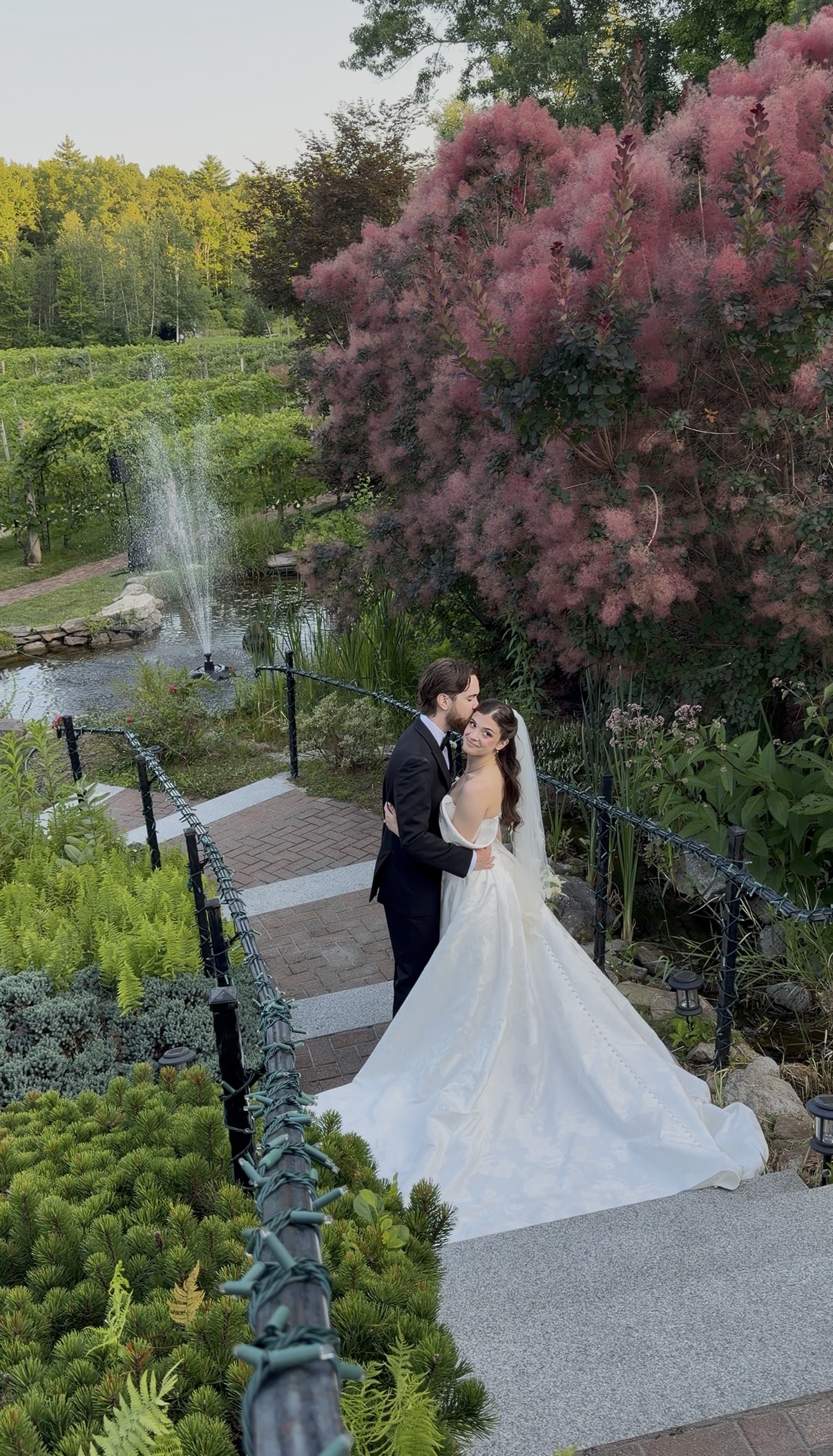 Groom kisses the bride's forehead on the stairs in front of the fountain.