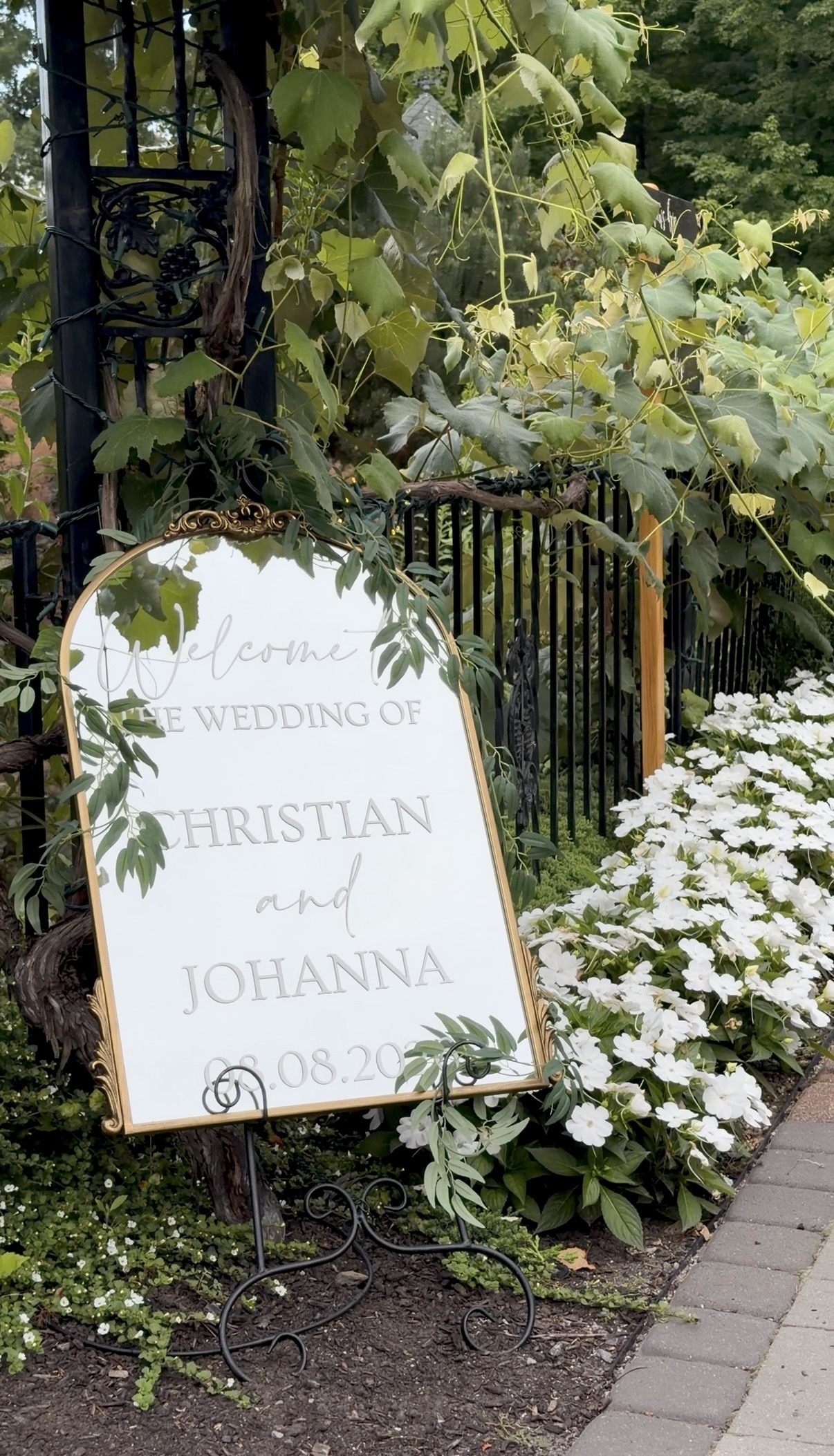 A gold-framed mirror greets guests at the garden gate, tucked in among the vines and summer blooms.