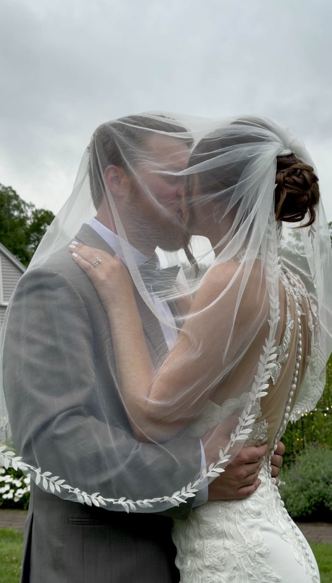 "Christie Raymond and Nick Millett kissing under the bride's veil at Zorvino Vineyards — summer wedding August 2026 Sandown NH"