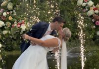 "Travel themed vineyard wedding at Zorvino Vineyards: Khyrstyne Quigley and Michael Pieroni kiss under floral arches at the pond as cold sparks rise behind them"