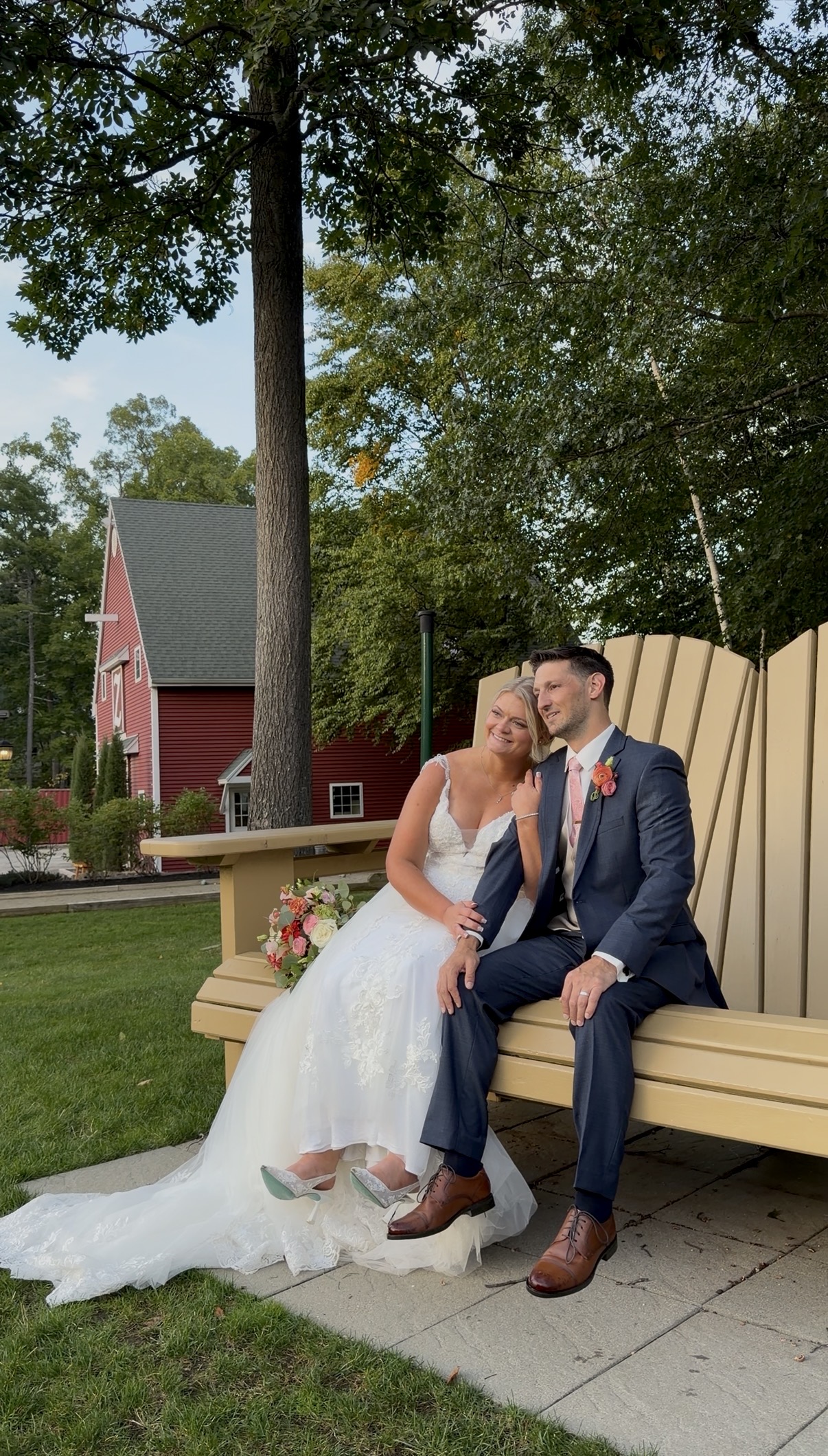 "Bride and groom sit together on a giant yellow Adirondack chair on the lawn at Zorvino Vineyards with the red Z barn behind them"