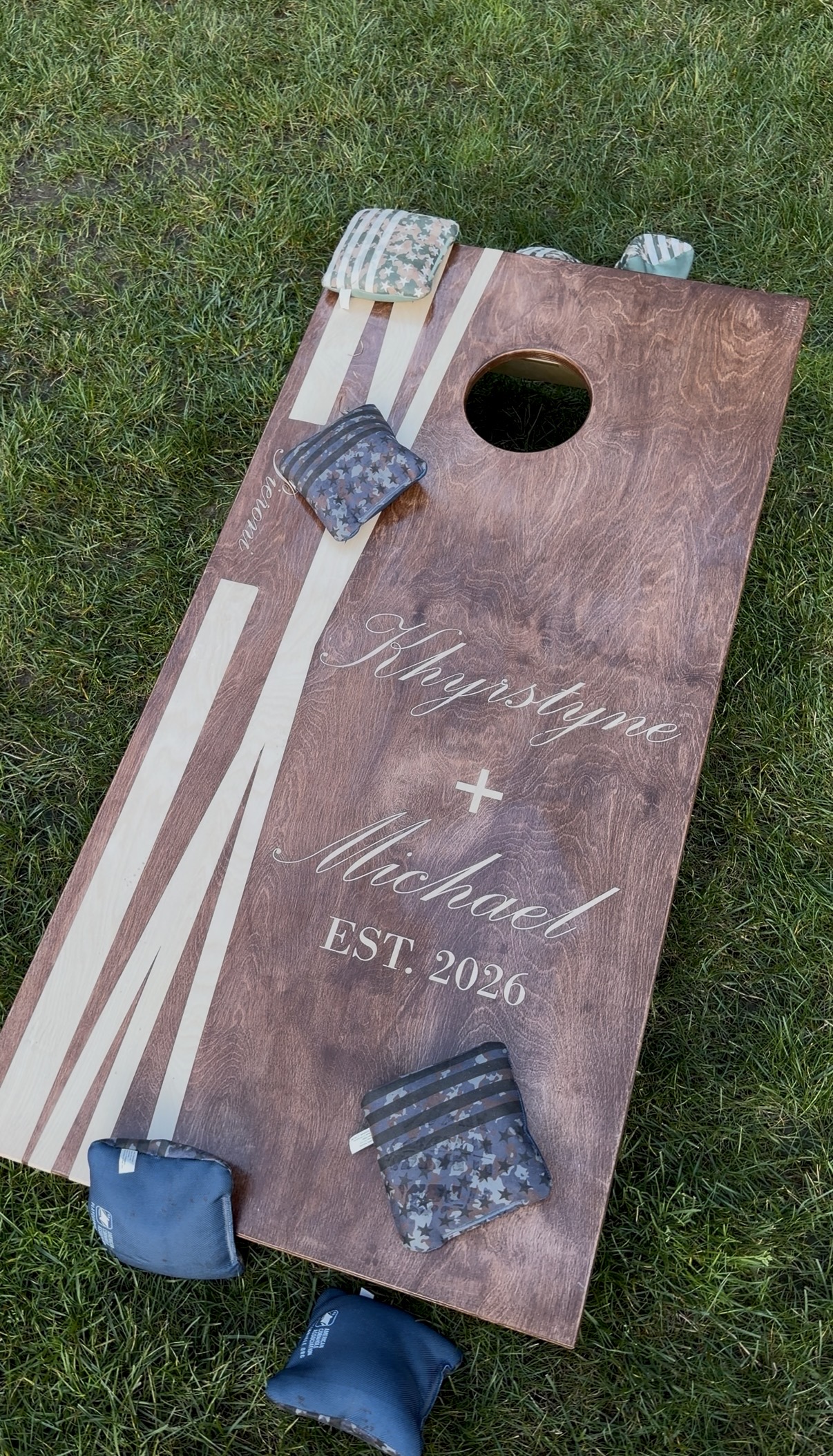"Custom wood cornhole board reading Khyrstyne plus Michael EST. 2026 on the lawn at Zorvino Vineyards with star-patterned bean bags"
