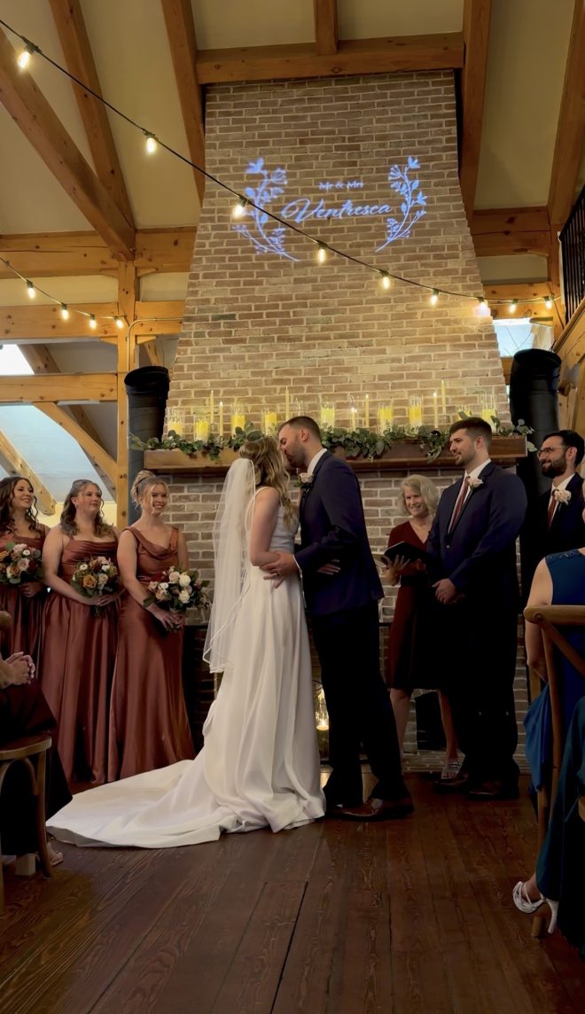 Mauve and navy vineyard wedding at Zorvino Vineyards: Meghan McDonnell and Alex Ventresca share their first kiss at the candlelit fireplace beneath a Mr. and Mrs. Ventresca monogram.