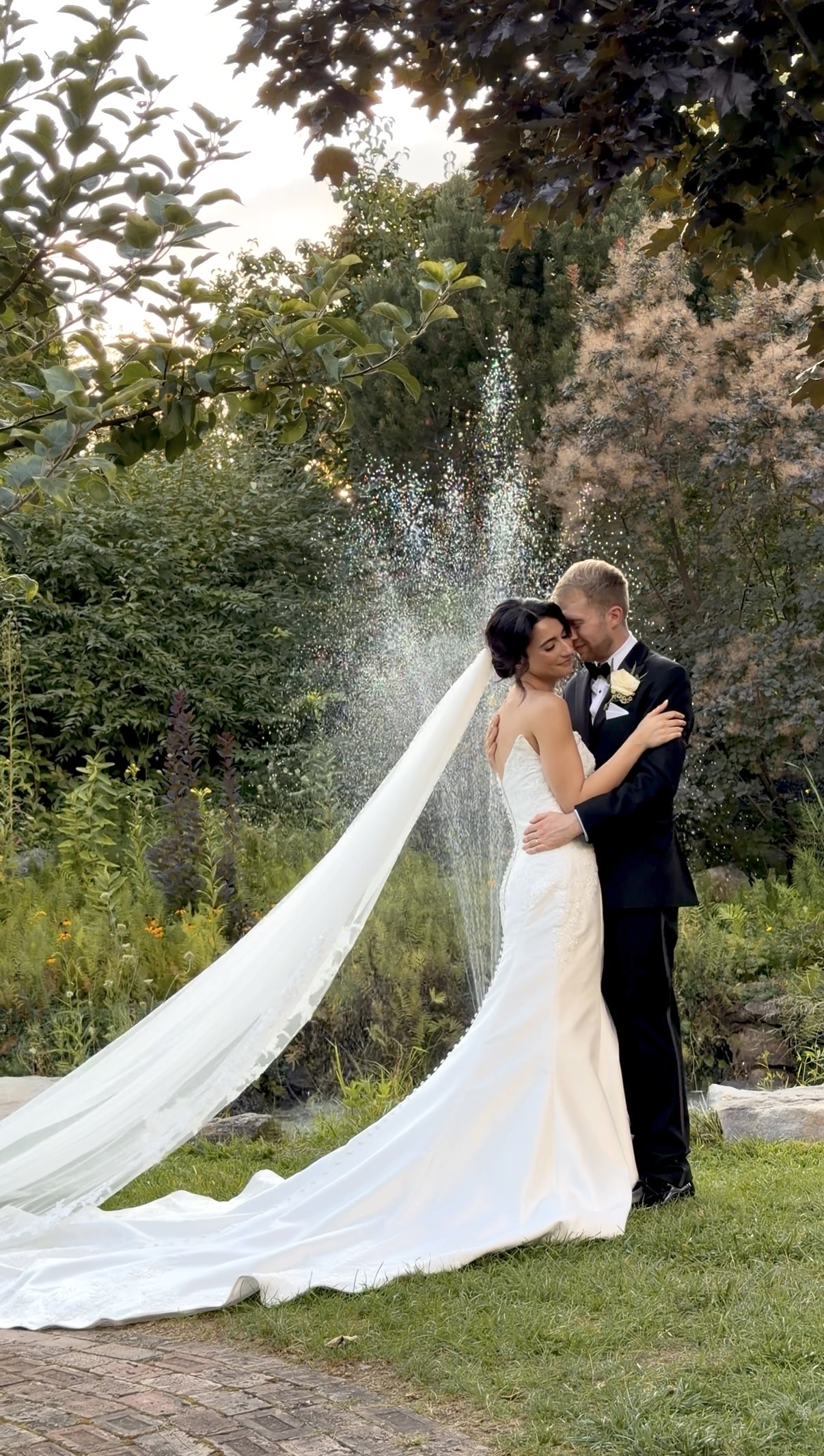 Bride and groom hold each other in front of a fountain in the garden.