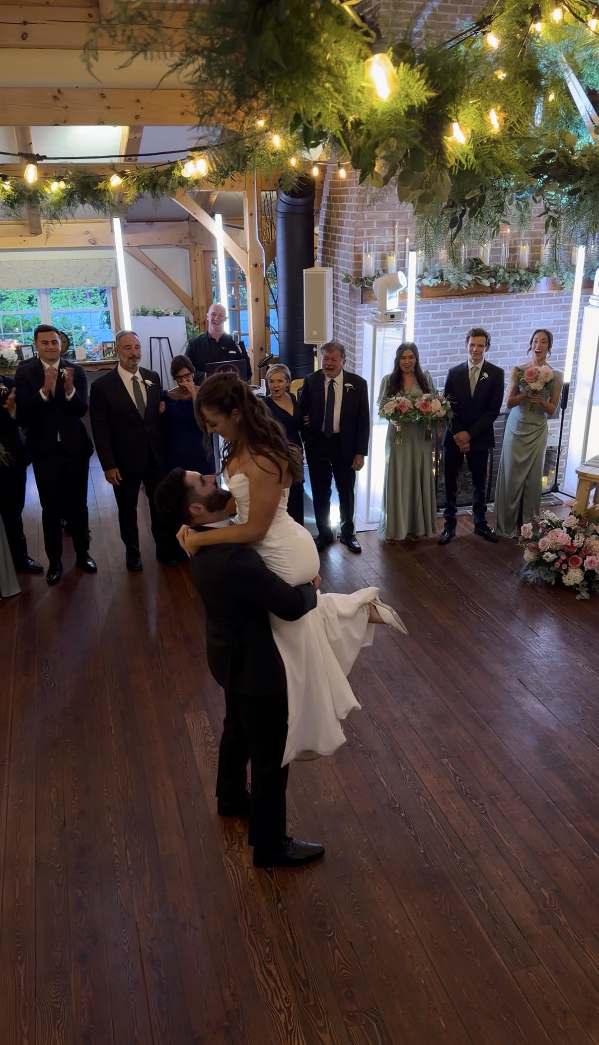 Jake lifts Annie during the first dance as the wedding party cheers them on.
