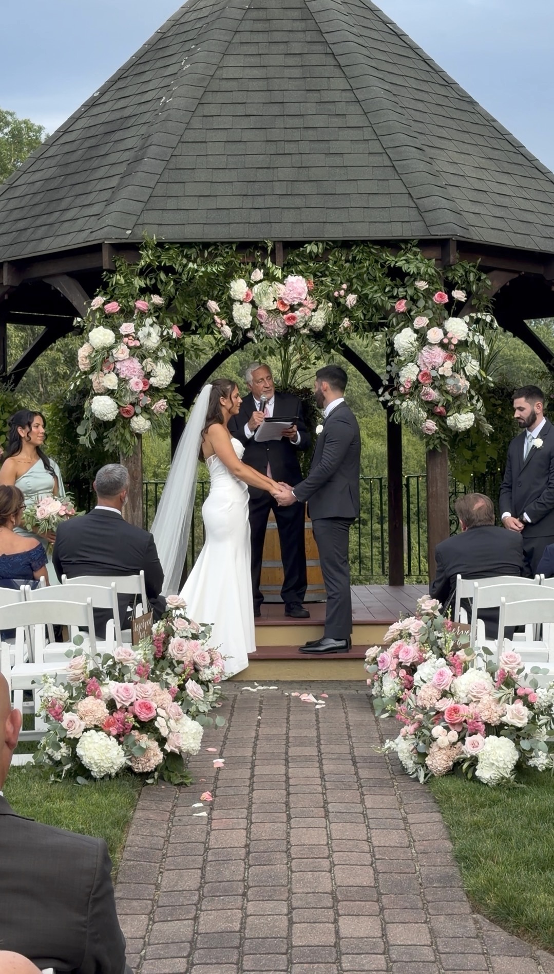 Vows at the flower-framed gazebo, the vineyard stretching out beyond.
