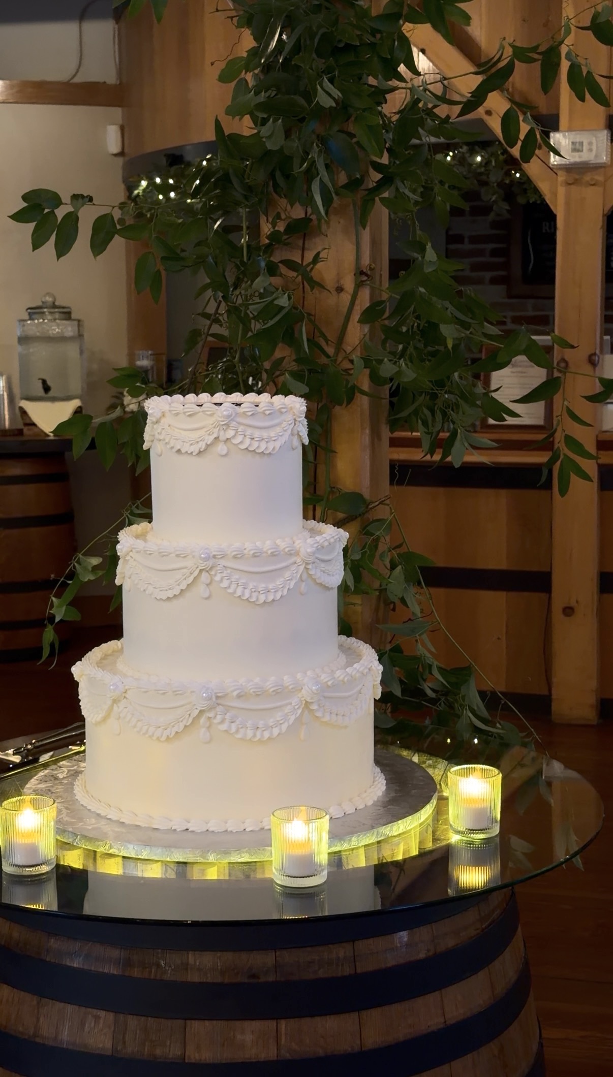 A three-tier ivory cake by Chickadee Hill Cakes, glowing on a candlelit wine barrel. 
