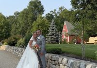 Elizabeth and Jeremy by the stone wall with Zorvino's red barn behind them at their family vineyard wedding in Sandown, NH