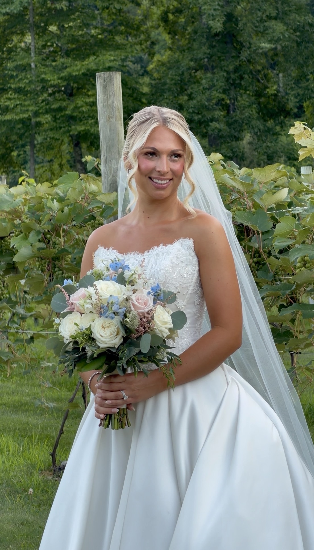 Bride holding a blush and dusty-blue bouquet in the vineyard rows at a summer garden vineyard wedding at Zorvino Vineyards