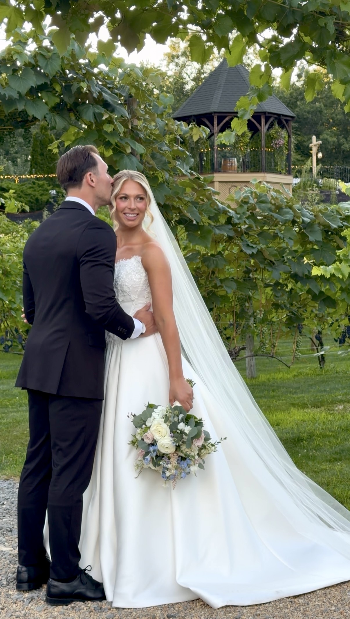 Bride and groom by the gazebo surrounded by grapevines at their summer garden vineyard wedding at Zorvino Vineyards