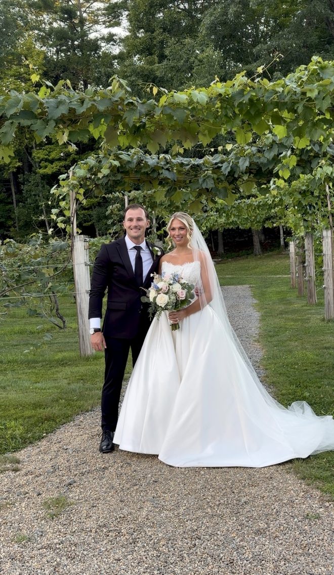 Lilly and Steven beneath Zorvino's grape arbor at their summer garden vineyard wedding in Sandown, NH